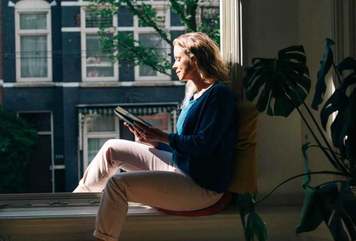 Vrouw zit thuis bij het raam met een boek