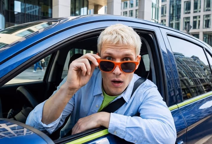 Een man kijkt over zijn zonnebril uit het zijraam van zijn auto