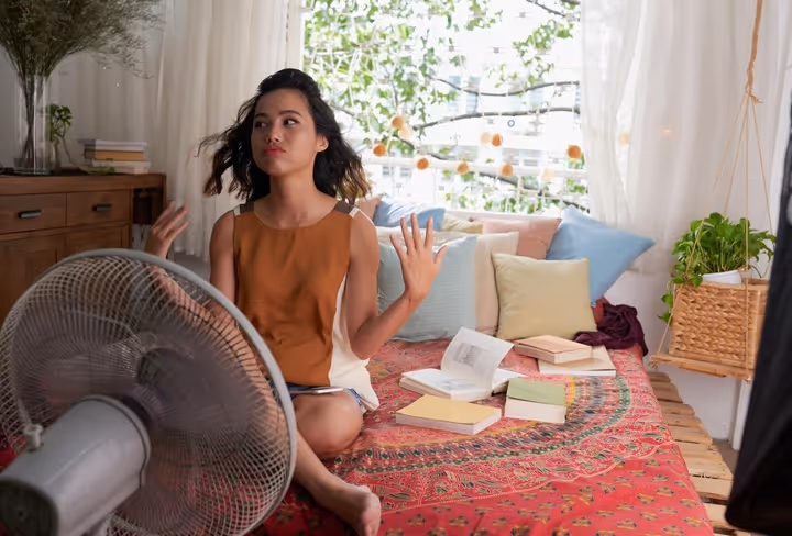 Een vrouw zit puffend van de warmte voor een ventilator 