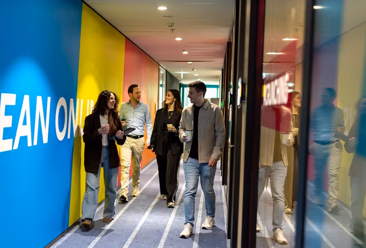 Een groep collega's loopt lachend door de gang in het Allianz Direct kantoor