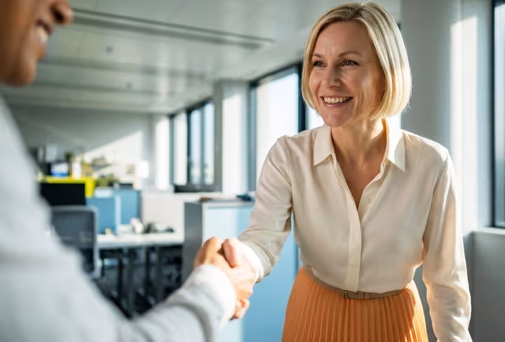 Een dame schudt vriendelijk lachend de hand van iemand die net buiten beeld staat. 