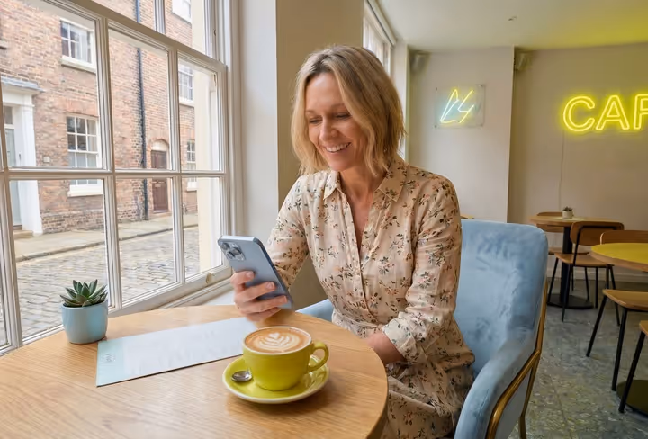 Een vrouw zit aan een tafeltje in een café met haar mobiel in haar hand