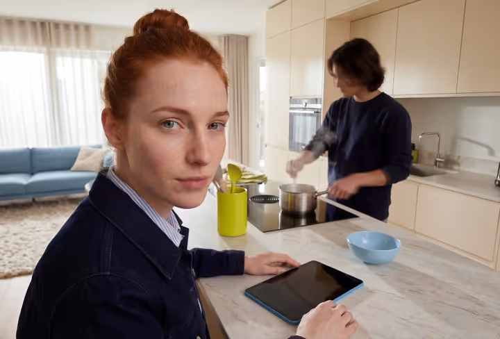 Een man en vrouw zitten aan het kookeiland in hun woning met een groot raam op de achtergrond
