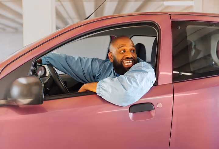Willie Wartaal zit in een roze auto en kijkt over zijn schouder uit het raam