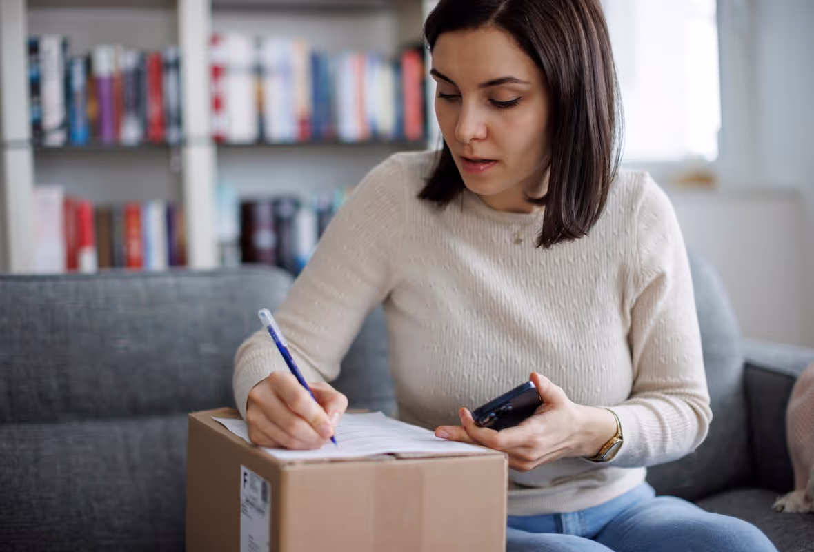 Een vrouw zit op de bank met een pakketje en ze schrijft iets op het label