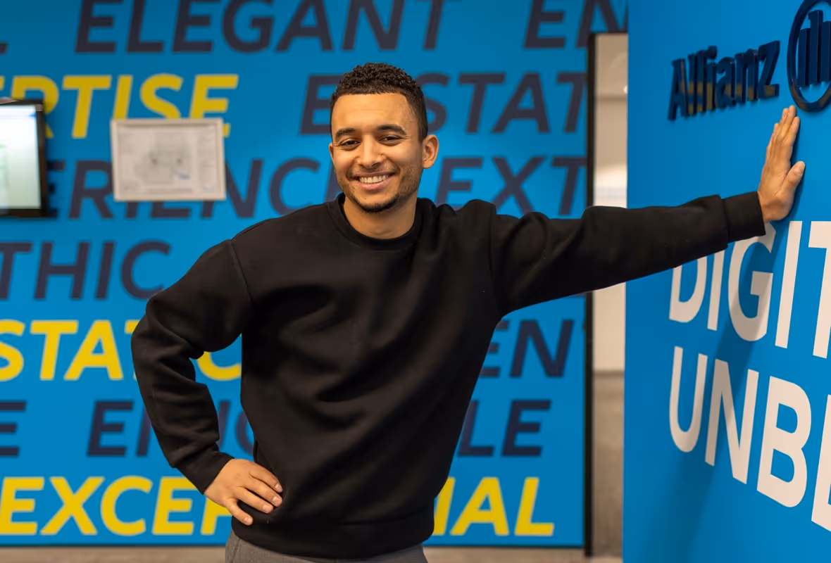 Garry Martes leunt met een hand tegen de muur en kijkt lachend de camera in.