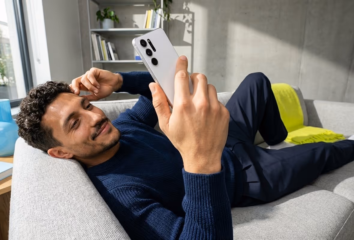 Een man ligt thuis op de bank met zijn mobiel in zijn hand