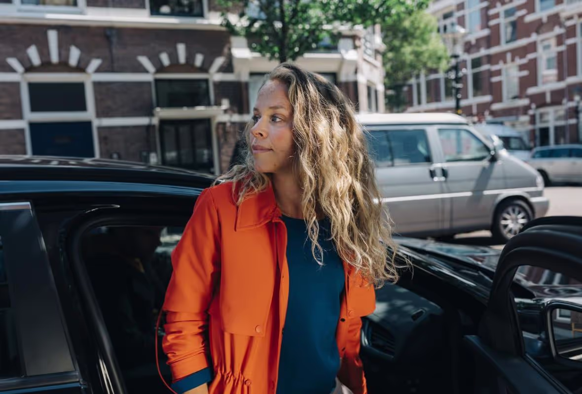 Vrouw met oranje jas bij grijze auto