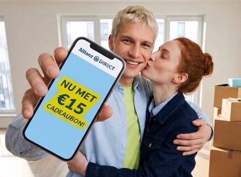 Een man en vrouw staan in een lege woonkamer met verhuisdozen. Zij geeft hem een kus en hij toont een smartphone waarop staat: "Nu met €15 cadeaubon!"