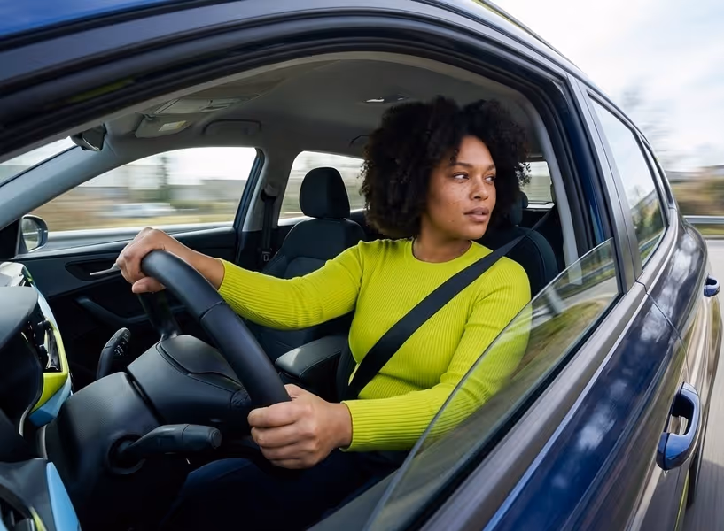 Een vrolijke vrouw zit in de auto en kijkt uit het autoraam