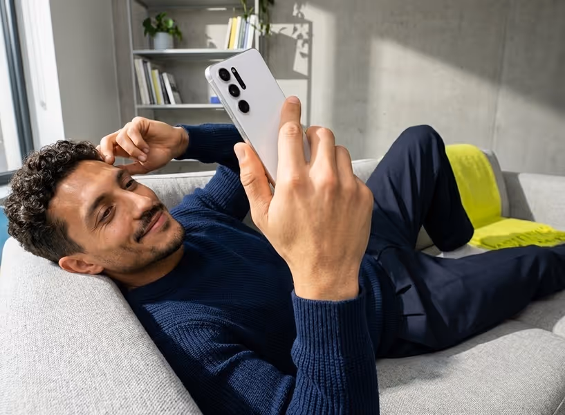 Een man ligt thuis op de bank met zijn mobiel in zijn hand