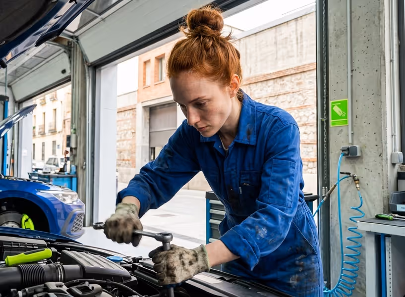 Een vrouwelijke automonteur staat te sleutelen onder de motorkap van een auto in de garage.