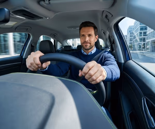 Een lachende man zit achter het stuur van een auto