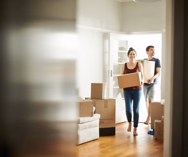 Een stel loopt lachend met verhuisdozen in een lege woning