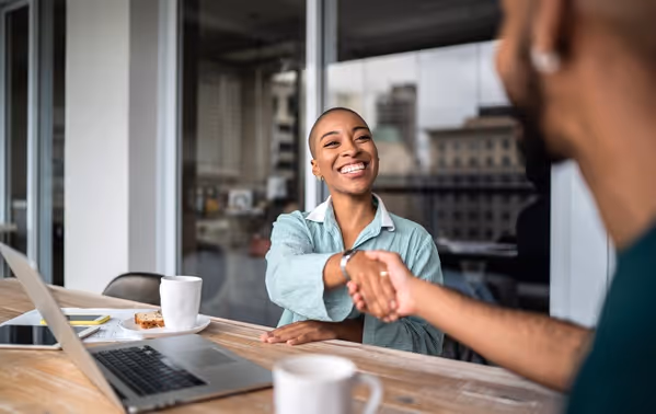 Een vrolijk lachende vrouw schudt de hand van iemand tegenover haar.
